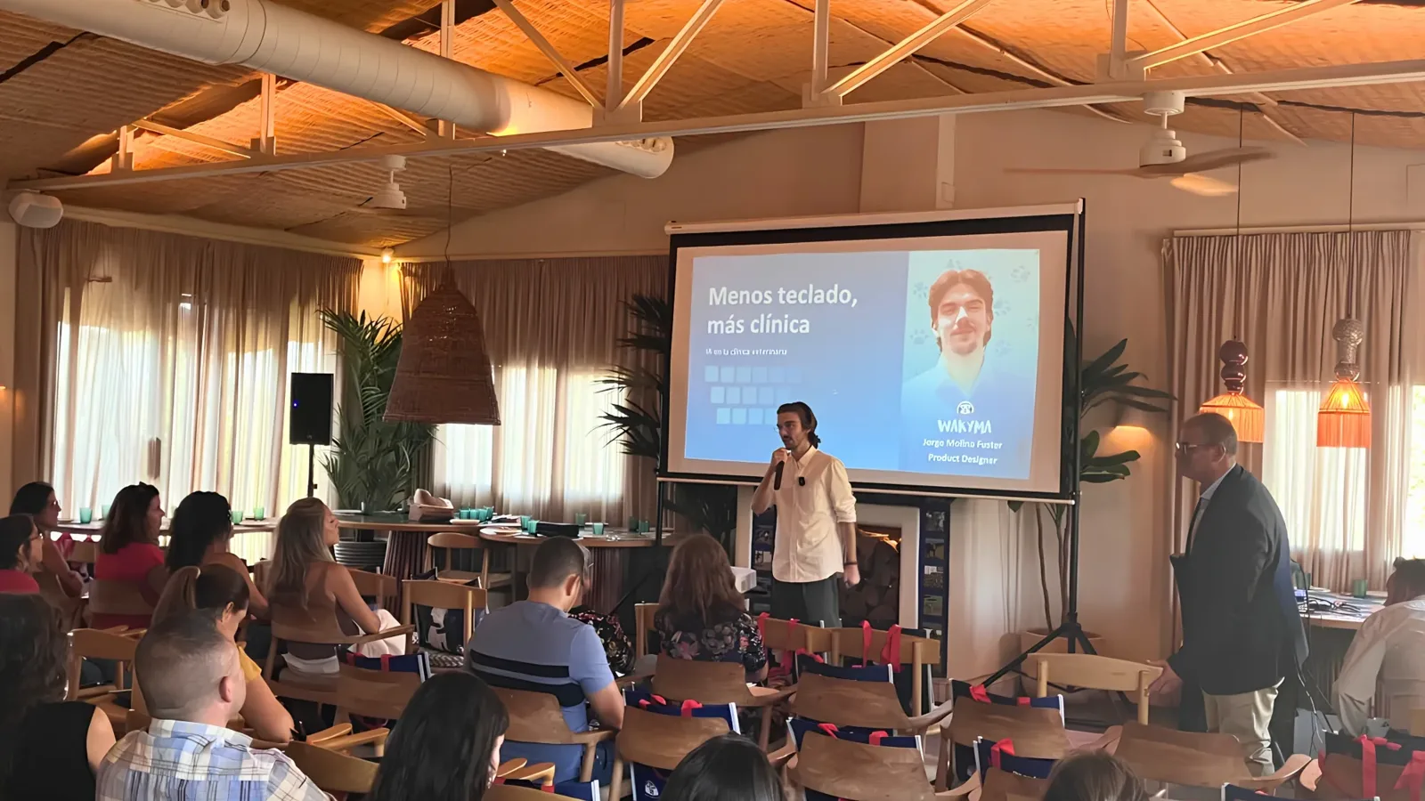 Jorge speaking with a microphone to a full room, in front of a slide titled "Menos teclado, más clínica" at the EVE26 event in Seville